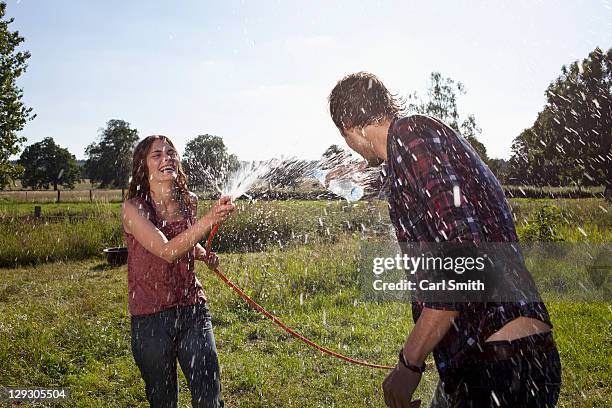 girl sprays guy with hose on field - hot wet men ストックフォトと画像