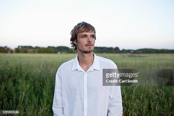 guy in white shirt looks to the side in field - naturbursche stock-fotos und bilder