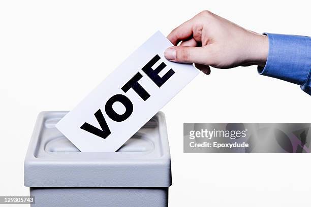 a man putting a ballot with the word vote written on it into a ballot box, close-up hands - vote ballot box stock pictures, royalty-free photos & images