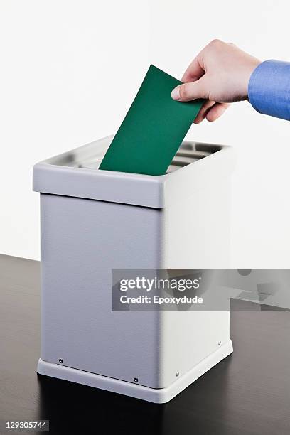 a man putting a blank green ballot into a ballot box, close-up hands - ballot box fotografías e imágenes de stock