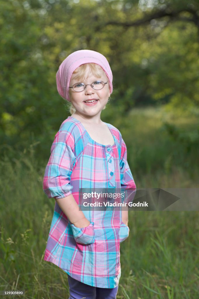 A young smiling girl with her hands in her pockets standing in nature