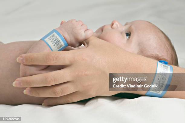 a baby holding her mother's thumb, both wearing hospital id bracelets - ziekenhuisidentificatiearmband stockfoto's en -beelden