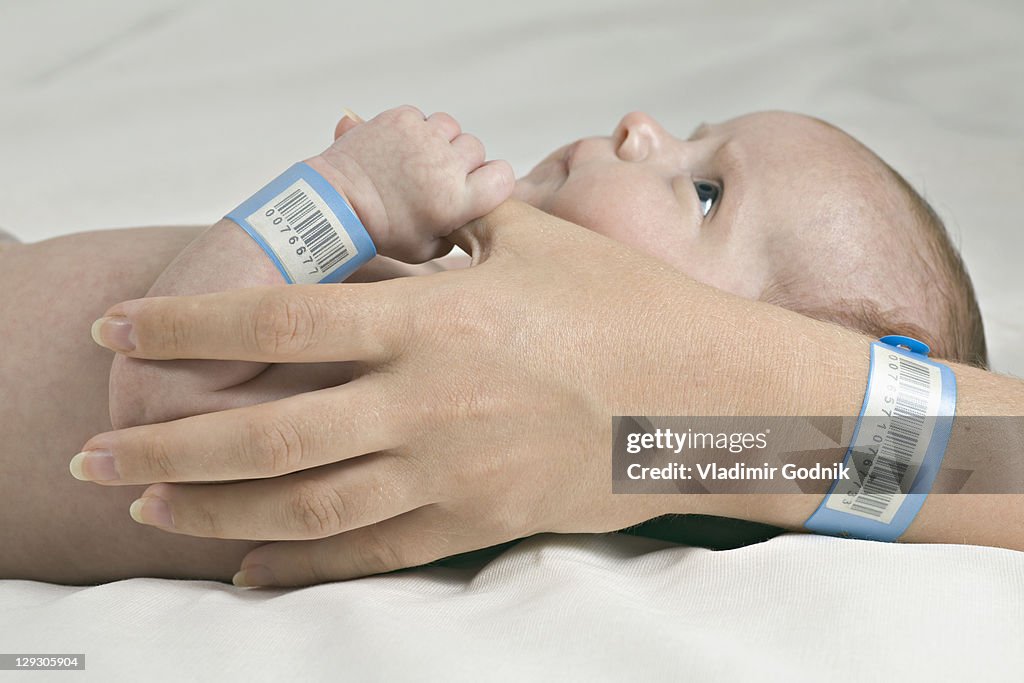 A baby holding her mother's thumb, both wearing hospital ID bracelets