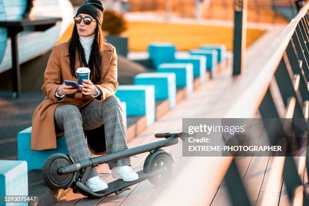 casual businesswoman seen after work in the public park using her cellphone and enjoying cup of tea - mobility scooter stock pictures, royalty-free photos & images
