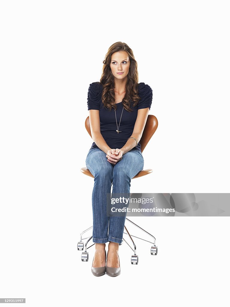 Studio shot of young woman sitting on chair with hands clasped