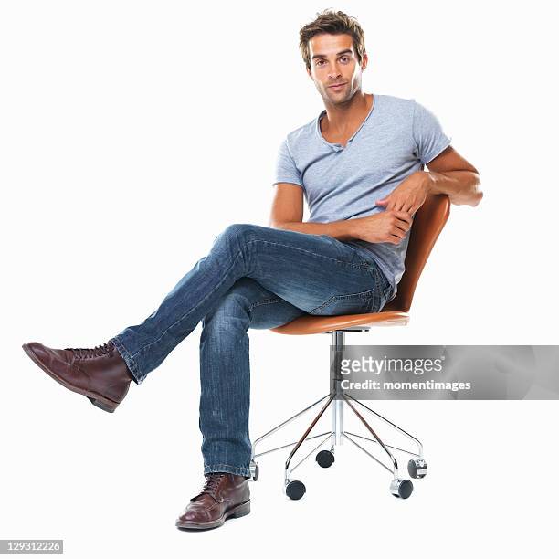 portrait of young man sitting on chair with legs crossed against white background - legs crossed at knee stock pictures, royalty-free photos & images