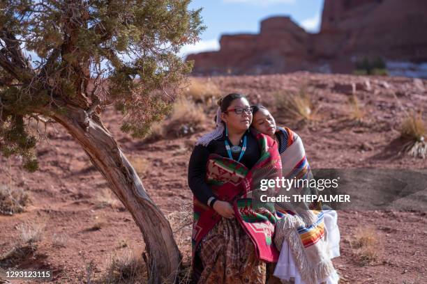 navajo siblings die op de boomstam van een kleine cederboom in de vallei van het monument zitten - arizona - native american reservation stockfoto's en -beelden