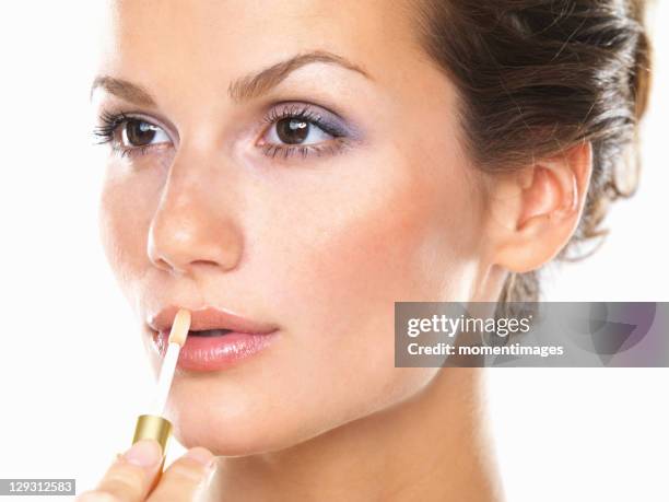 studio portrait of beautiful woman applying lip gloss - gloss de labios fotografías e imágenes de stock