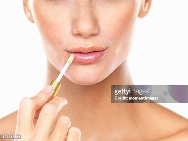 studio portrait of beautiful woman applying lip gloss - gloss stockfoto's en -beelden
