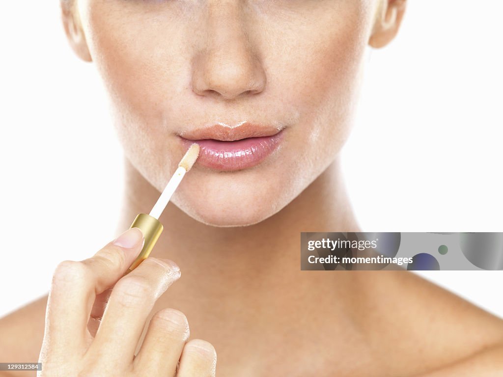 Studio portrait of beautiful woman applying lip gloss