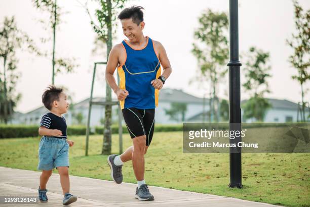 asian chinese smiling father and his son running togethers in the public park during weekend morning - determination kids stock pictures, royalty-free photos & images