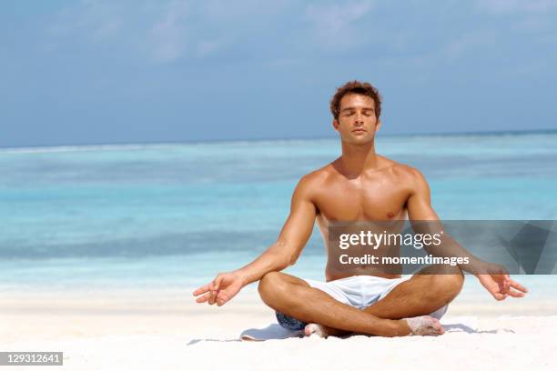 maldives, handsome young man meditating in a lotus position on the beach - semi dress stock pictures, royalty-free photos & images