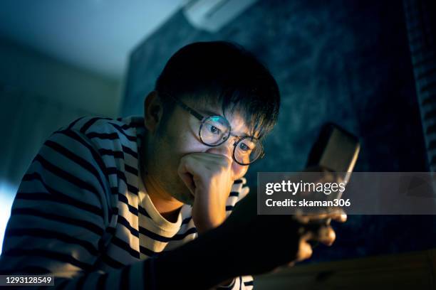 asian man young adult feeling worried and concerned after use smartphone on the bed - young man to bed photos et images de collection