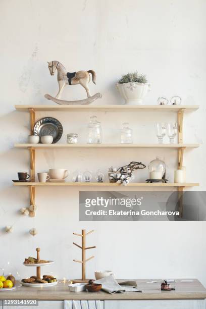 beautiful design of the white wall in the kitchen. shelves on the wall with a beautiful decor. warm and cozy in the kitchen. kitchen set with christmas decor. vase, spruce branches, cones, candles. - kitchen shelves stock pictures, royalty-free photos & images