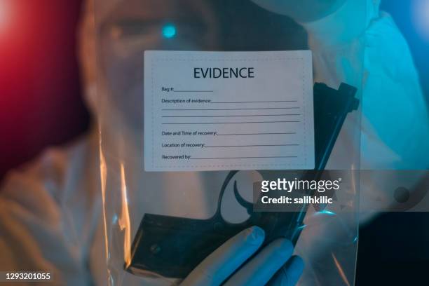 a male forensic scientist holding an evidence bag which contains 9mm pistol - coroner stock pictures, royalty-free photos & images