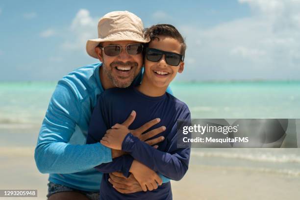 retrato de padre e hijo en playa tropical - sombrero de sol fotografías e imágenes de stock