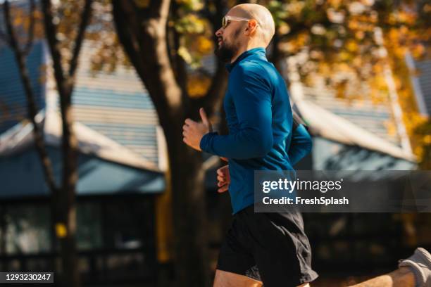 rotina matinal: atleta bonito correndo no parque em um dia de outono - vista lateral - calções azuis - fotografias e filmes do acervo