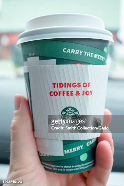 Close-up of Starbucks coffee holiday cup design in human hand, with text reading Tidings of Coffee and Joy, Walnut Creek, California, December 21,...