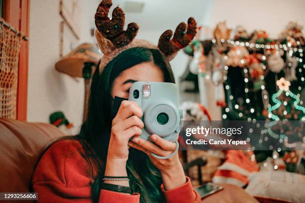 female teenager taking pictures with instant camera in xmas time at home - foto shooting stock-fotos und bilder