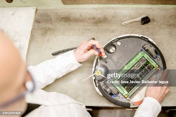 anonymous maure man in and white work coat repairing a vacuum cleaning irobot in a small, simple workshop - aspirapolvere foto e immagini stock