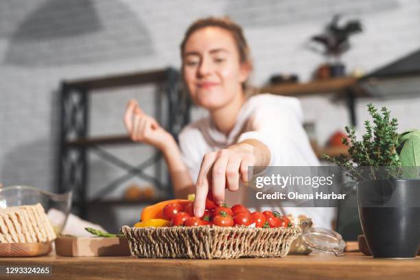 young beautiful girl reaches for cherry tomatoes on the kitchen table - cherry tomatoes stock-fotos und bilder