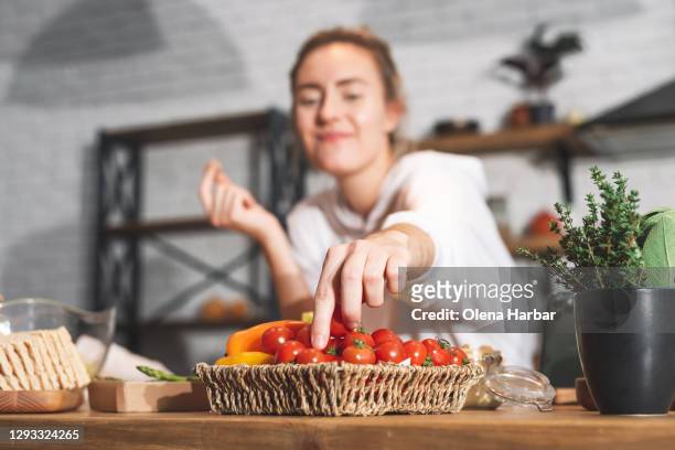 young beautiful girl reaches for cherry tomatoes on the kitchen table - cherry tomatoes stock pictures, royalty-free photos & images