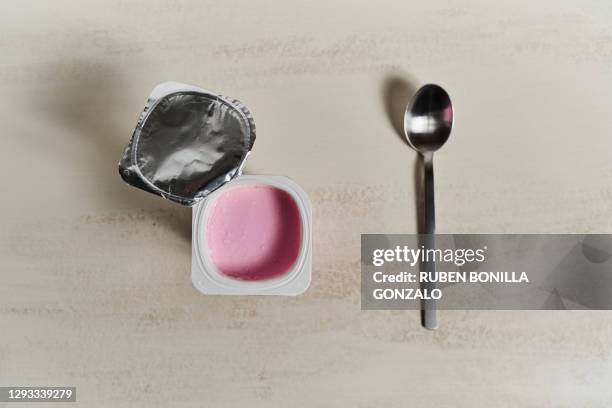 above view of a empty metallic spoon and a red yoghurt cup made of plastic on white backgrounds. horizontal photo. - joghurtbecher stock-fotos und bilder