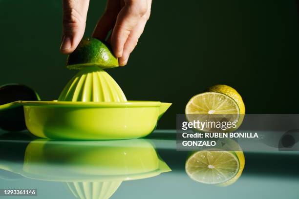 front view of a hand squeezing some green citric limes, some of them are cut in two halves, and a juicer to squeeze them with reflection on the glass mirror of a table. horizontal photo - saftpresse stock-fotos und bilder
