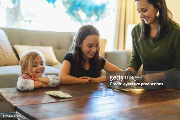 millennial vrouwelijke moeder met tiener en pre school leeftijd dochters omgaan met geld - zakgeld stockfoto's en -beelden