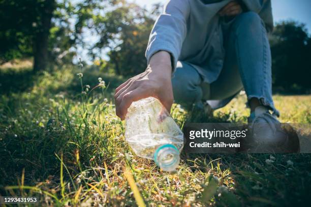 mujer mano sosteniendo botella de basura plástico poner en bolsa de reciclaje para la limpieza - plucking fotografías e imágenes de stock