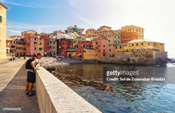 tourist man with backpack on his back traveling with his teenage daughter looking at the sea in boccadasse, genoa, italy - genoa stock-fotos und bilder