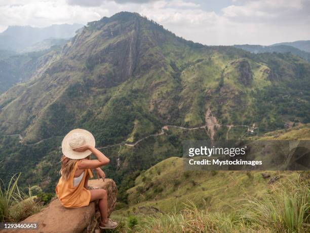 young woman sitting on rock on top of beautiful mountain range in sri lanka admiring the green lush landscape - adams peak stock pictures, royalty-free photos & images
