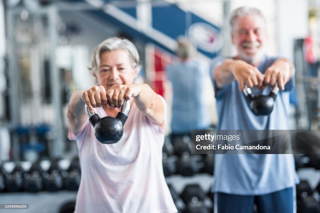 Couple of two happy and fitess seniors doing exercise in the gym together running on the tapis roulant - active lifestyle