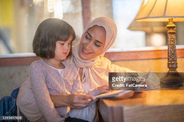 muslim mother and daughter reading together - lebanese ethnicity stock pictures, royalty-free photos & images