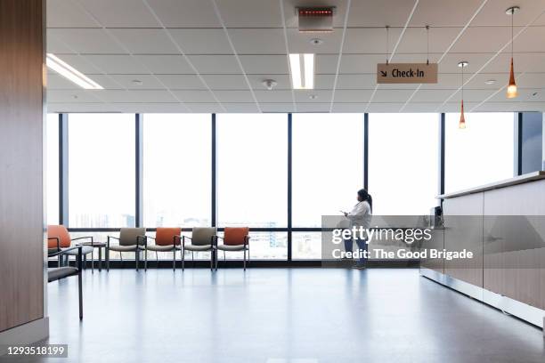 side view of doctor with digital tablet standing against window in hospital - waiting room stock pictures, royalty-free photos & images