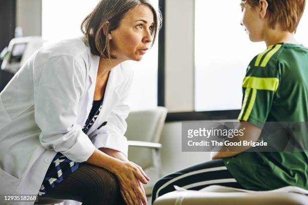 smiling doctor talking to boy in exam room - doctor listener imagens e fotografias de stock