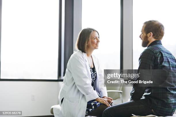 female doctor in discussion with male patient in exam room - examen médico fotografías e imágenes de stock