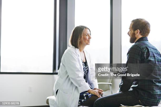 female doctor in discussion with male patient in exam room - male doctor man patient stock pictures, royalty-free photos & images