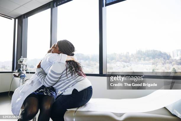 doctor embracing young woman while sitting on bed in hospital - emotional support stock pictures, royalty-free photos & images
