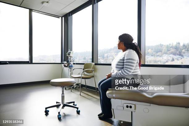 side view of female patient sitting on bed in hospital - examination room imagens e fotografias de stock
