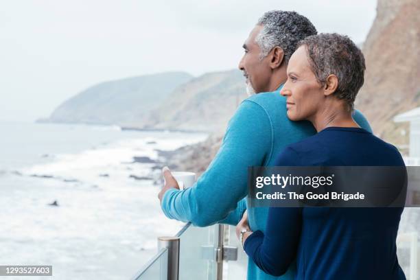 rear view of mature couple looking at sea while standing on balcony - femmes de dos enlacée photos et images de collection