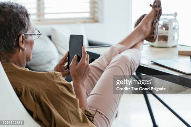 woman using mobile phone while sitting at desk in home office - feet up stock pictures, royalty-free photos & images