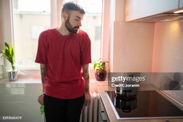 junger mann wartet auf wasser in der pfanne zu kochen - glaskeramik stock-fotos und bilder