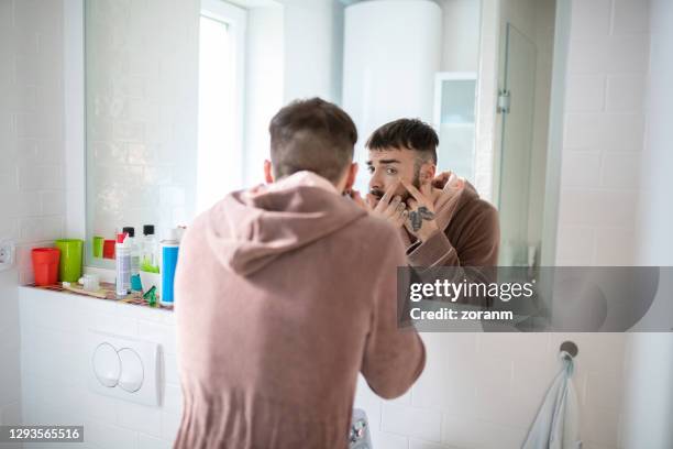 junger mann im bademantel vor dem badezimmerspiegel quetscht mitesser - blackhead stock-fotos und bilder