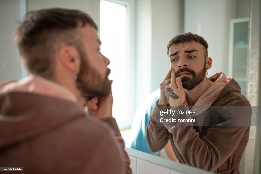 Young man in bathrobe squeezing blackhead on his cheek