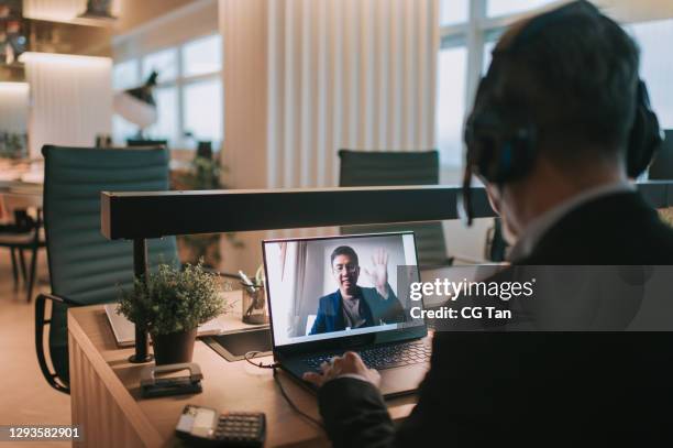 asian chinese mature businessman with beard typing and replying email to his customer and video call with his client in the office using laptop - two people video conferencing stock pictures, royalty-free photos & images