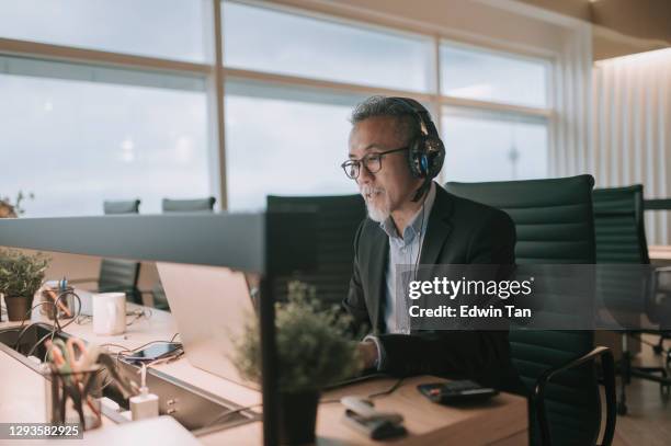 asian chinese mature businessman with beard typing and replying email to his customer and video call with his client in the office using laptop - computer headset stock pictures, royalty-free photos & images