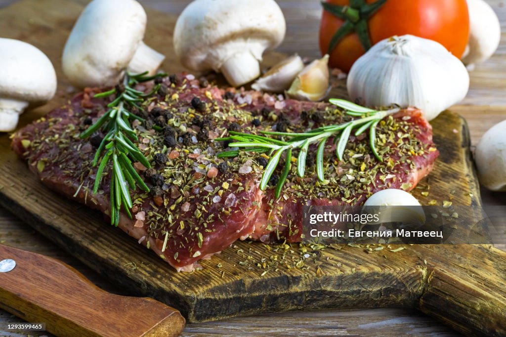Raw beef steak served with vegetables and herbs on rustic wooden board background