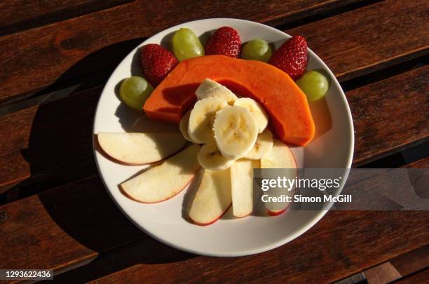 fruit salad plate of apple, banana, papaya, strawberries and green grapes on a wooden table top - apple plate stock pictures, royalty-free photos & images