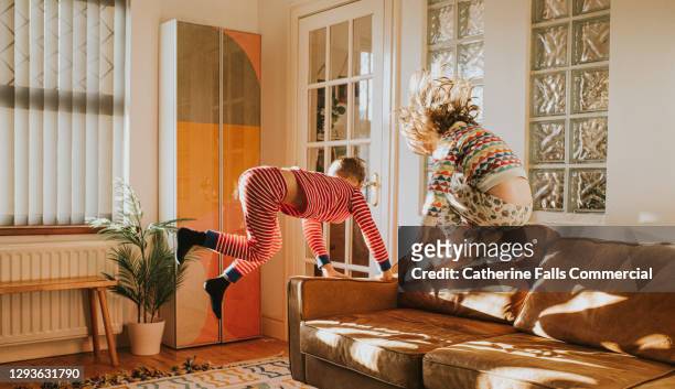children bouncing on a brown leather sofa in a sunny domestic room - giochi per bambini foto e immagini stock
